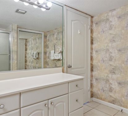 Step into your private bathroom featuring elegant marble-style walls, bright vanity lighting, and a spacious glass-enclosed shower for your comfort.