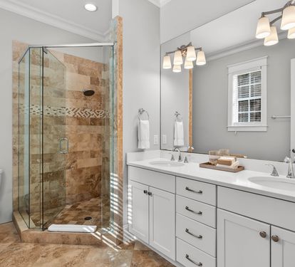 Your spacious bathroom features dual vanities, a luxurious glass-enclosed shower with mosaic accents, and elegant fixtures for your comfort.