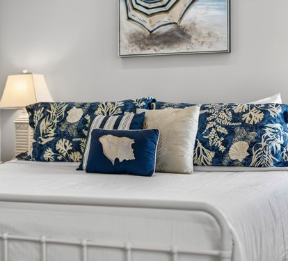 Sink into crisp white linens adorned with coastal-inspired blue pillows, where soft lamplight creates the perfect reading ambiance.