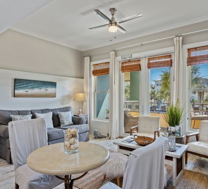 Stylish and sunlit 30A retreat with comfy seating, chic coastal décor, and floor-to-ceiling windows leading to a private balcony with palm views—ideal for relaxing in beachside comfort.