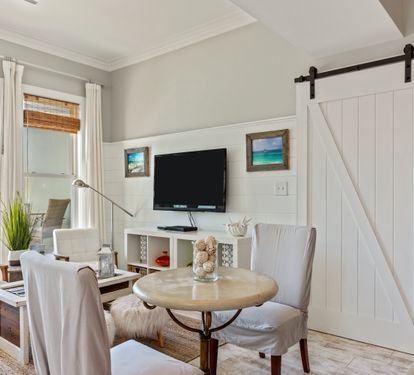 Coastal-inspired nook with a wall-mounted TV, round dining table, and stylish barn door—blending charm and comfort for a perfect 30A retreat.