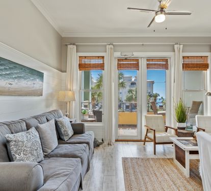 Cozy 30A living space with plush seating, beachy décor, and sunlit French doors leading to a balcony with tropical views—perfect for laid-back coastal living.