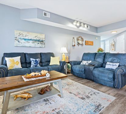 Sink into plush blue recliners in your spacious living room, where coastal artwork and warm lighting create the perfect retreat.