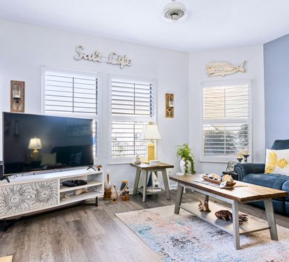 Unwind in your coastal-themed living room with plush seating, charming nautical touches, and natural light streaming through plantation shutters.
