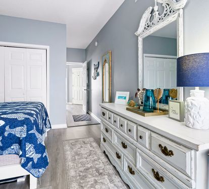 Your serene bedroom features soothing blue walls, elegant white furniture, and thoughtful coastal touches that create the perfect retreat for relaxation.