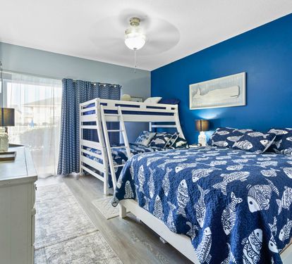 Unwind in this vibrant blue bedroom featuring comfortable bunk beds and a queen bed, perfect for families seeking coastal-themed comfort.