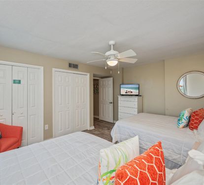 Unwind in your bright bedroom featuring two comfortable beds, vibrant coral accents, and entertainment for perfect vacation relaxation.