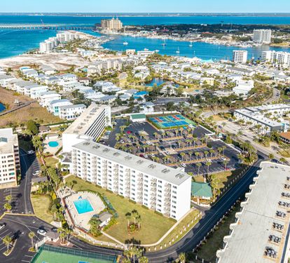 Aerial view of a waterfront resort community featuring white buildings, pools, and marina access in a stunning coastal setting.