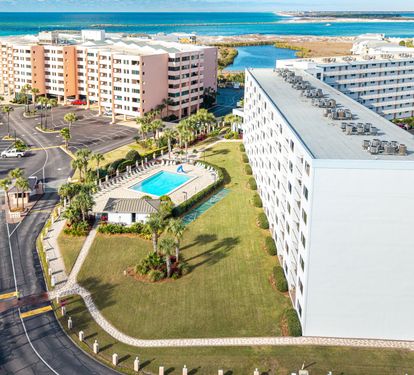 Aerial view of beachfront resort complex with multiple buildings, swimming pool, and direct beach access along turquoise waters.