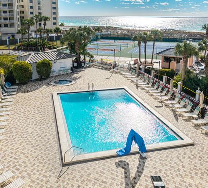 Beachfront resort pool area featuring multiple swimming pools, hot tub, tennis courts, and direct beach access with palm trees.