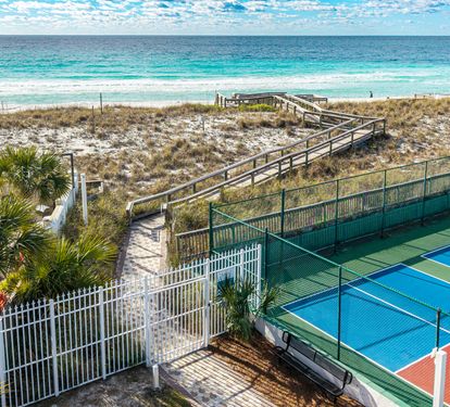 Beachfront resort featuring tennis court and direct beach access via wooden boardwalk through pristine sand dunes.