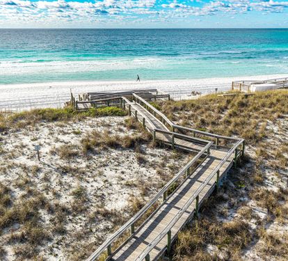 Pristine white sand beach with wooden boardwalk leading to turquoise waters and endless ocean views.