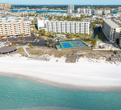 Beachfront resort complex with pristine white sand beach, tennis courts, and multiple accommodation buildings along the Gulf Coast.