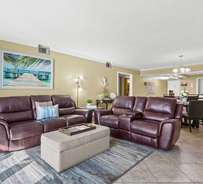 Relax in your spacious living room with plush leather recliners and tropical artwork creating the perfect coastal retreat atmosphere.