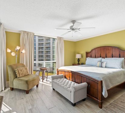 Relax in your spacious bedroom with rich wood furnishings, cozy seating, and bright city views from floor-to-ceiling windows.