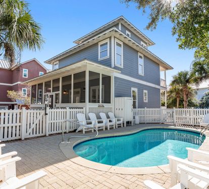 Charming coastal home with private pool surrounded by palm trees and white picket fence for your perfect beach getaway.