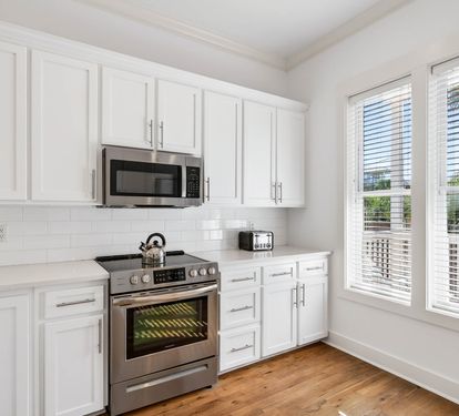 Your fully equipped kitchen features crisp white cabinets, stainless steel appliances, and warm hardwood floors, creating the perfect space for preparing home-cooked meals.