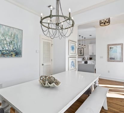 Gather around your elegant dining table beneath the stunning chandelier, where coastal artwork and warm hardwood floors create the perfect setting for memorable meals.