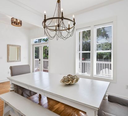 Gather around your elegant dining table where warm wood floors meet crisp white walls and natural light streams through French doors.