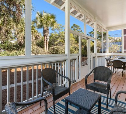 Your screened porch offers peaceful moments with wicker seating and tropical palm views through tall windows.
