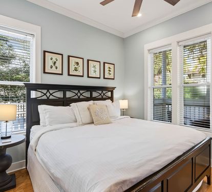 Wake up in your serene bedroom where soft morning light filters through windows, illuminating crisp white linens on your elegant wooden bed.