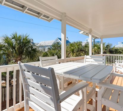 Step onto your private covered deck where white dining furniture awaits under swaying palm trees and coastal views.