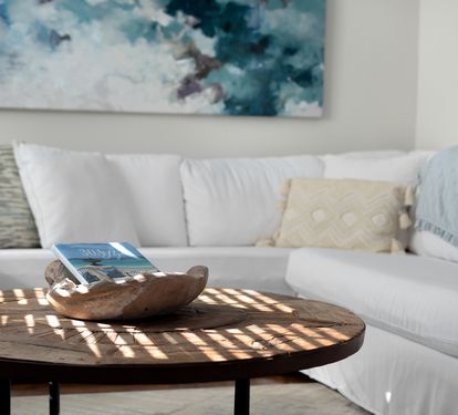 Sink into this plush sectional sofa where natural light creates dancing shadows across the rustic coffee table—your perfect spot for morning coffee and quiet moments.