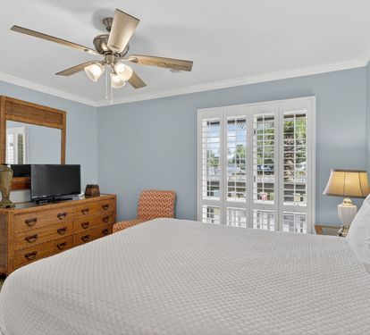 Relax in your serene bedroom featuring soothing blue walls, a comfortable bed with crisp linens, and French doors opening to your private balcony with outdoor views.