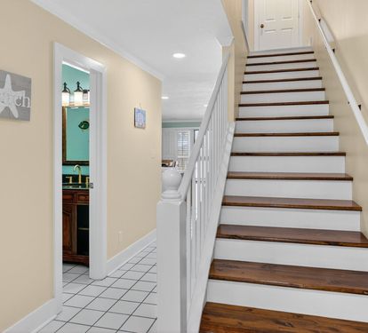 Ascend the beautiful wooden staircase to your upper level, with glimpses of the charming kitchen awaiting your culinary adventures below.