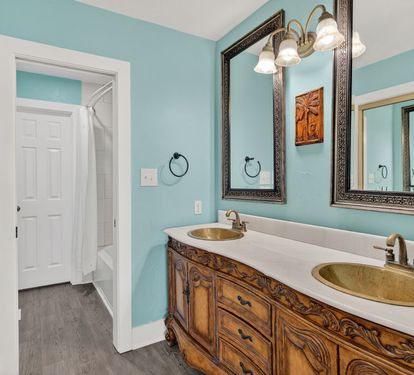 Your elegant bathroom features dual vanity sinks with ornate wooden cabinetry and soothing turquoise walls for a refreshing start to your day.