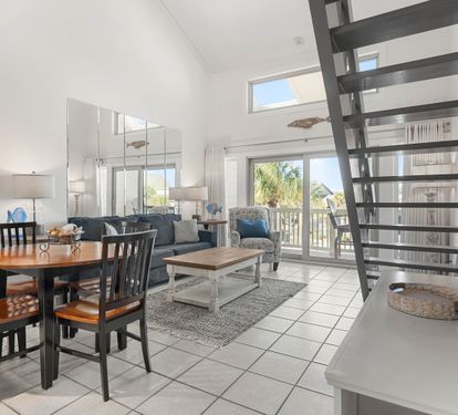 Your bright coastal retreat features an open-plan living space with ocean-inspired decor, comfortable seating, and large windows flooding the room with natural light.