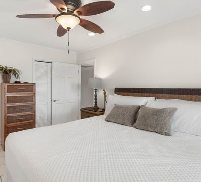 Drift off in your peaceful bedroom with crisp white linens, natural wicker headboard, and cooling ceiling fan for perfect comfort.
