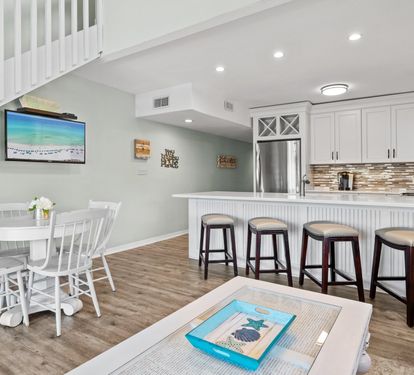 Bright coastal dining and kitchen area with bar seating, updated finishes, and an open-concept layout perfect for gathering, dining, and relaxing during your beach getaway.