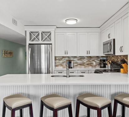 Beautifully updated coastal kitchen with quartz-style countertops, stainless steel appliances, and bar seating perfect for casual dining, morning coffee, or gathering after the beach.