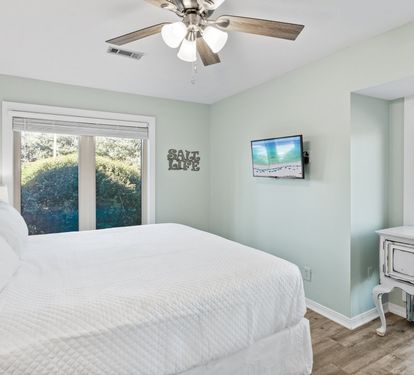 Relax in the primary bedroom featuring a king-size bed, coastal décor, natural light, and a peaceful atmosphere designed for restful nights after beach adventures.