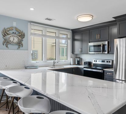 Modern kitchen with sleek dark cabinets, stainless steel appliances, and a large marble island with barstool seating for five—perfect for cooking, dining, and gathering with family and friends.