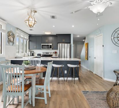 Open-concept dining and kitchen area with a coastal vibe features a round table for four, bar seating for five, and modern finishes—ideal for meals and memories with family and friends.
