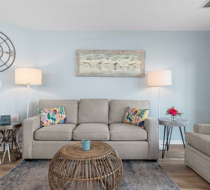 Charming coastal living room with a comfy sofa, beachy artwork, rattan coffee table, and soft blue walls—perfect for unwinding after a sunny day at the beach.