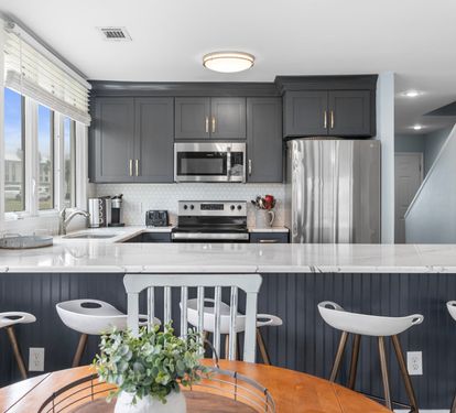 Bright and modern kitchen with sleek navy cabinets, quartz counters, and stainless appliances—bar seating and a cozy dining nook complete the perfect space for gathering.