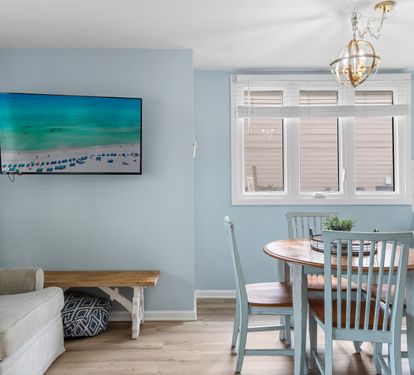 Cozy dining nook with a round wooden table, seafoam chairs, and a widescreen TV —perfect for casual meals or family game nights.
