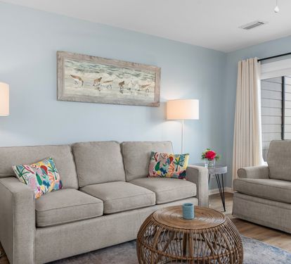 Cozy coastal living room with a plush sofa, tropical accent pillows, rattan coffee table, and beach-themed wall art—perfect for relaxing after a day in the sun.