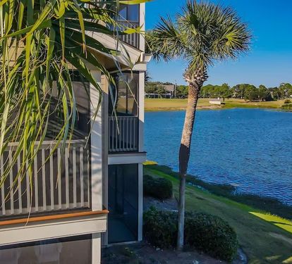 Screened balcony overlooks a peaceful lake lined with palm trees, offering the perfect spot to unwind and enjoy the serene, coastal surroundings.