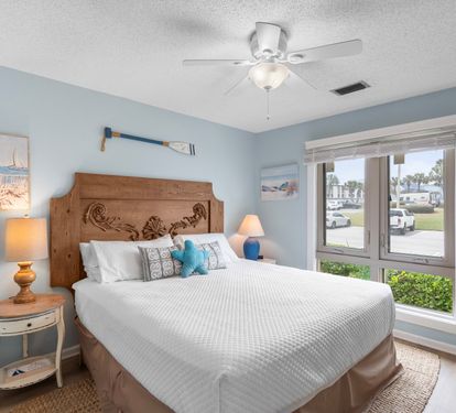 Guest bedroom with soft coastal colors, plush bedding, and charming nautical décor. Large windows brighten the space, creating a cozy and inviting retreat for friends or family.