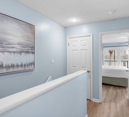 Upstairs hallway with soft coastal tones and wood flooring leads to serene bedrooms—creating a calm transition between living and sleeping spaces.