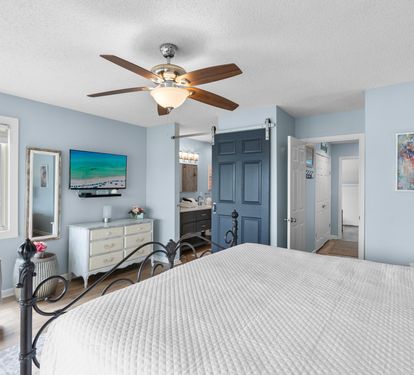Primary bedroom features a king bed, wide-screen TV, and en-suite bath with a stylish barn door—combining comfort, privacy, and coastal charm in one relaxing space.
