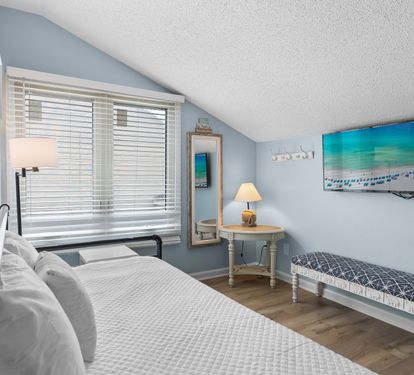 Bright and airy guest loft with a convertible daybed, wall-mounted TV, reading nook, and coastal décor—offering comfort and flexibility in a tranquil upstairs retreat.