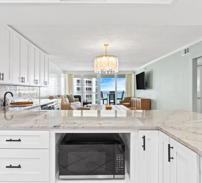 Your gourmet kitchen features gleaming marble countertops and elegant white cabinetry, perfect for preparing meals while enjoying ocean views.