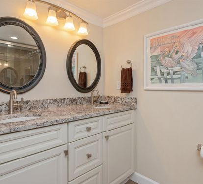 Refresh yourself in this elegant dual-vanity bathroom featuring granite countertops, warm lighting, and thoughtful coastal artwork to brighten your morning routine.