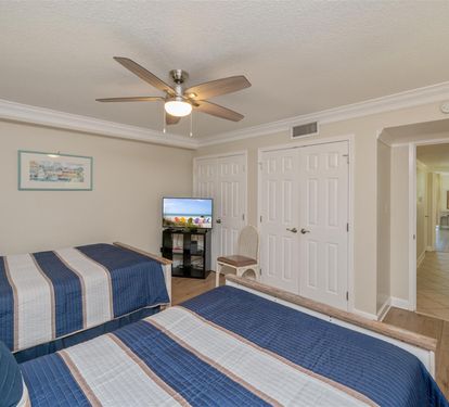 Relax in this comfortable twin bedroom featuring nautical blue bedding, ceiling fan, and TV for your entertainment.