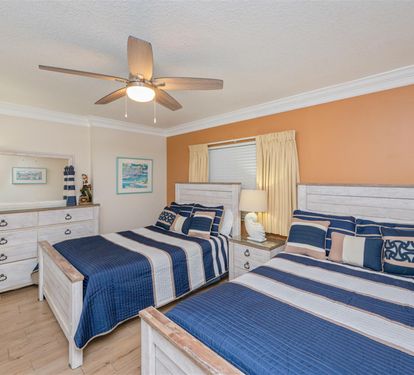 Your coastal bedroom features two comfortable beds with nautical linens, white furnishings, and warm orange accent walls creating a relaxing seaside retreat.